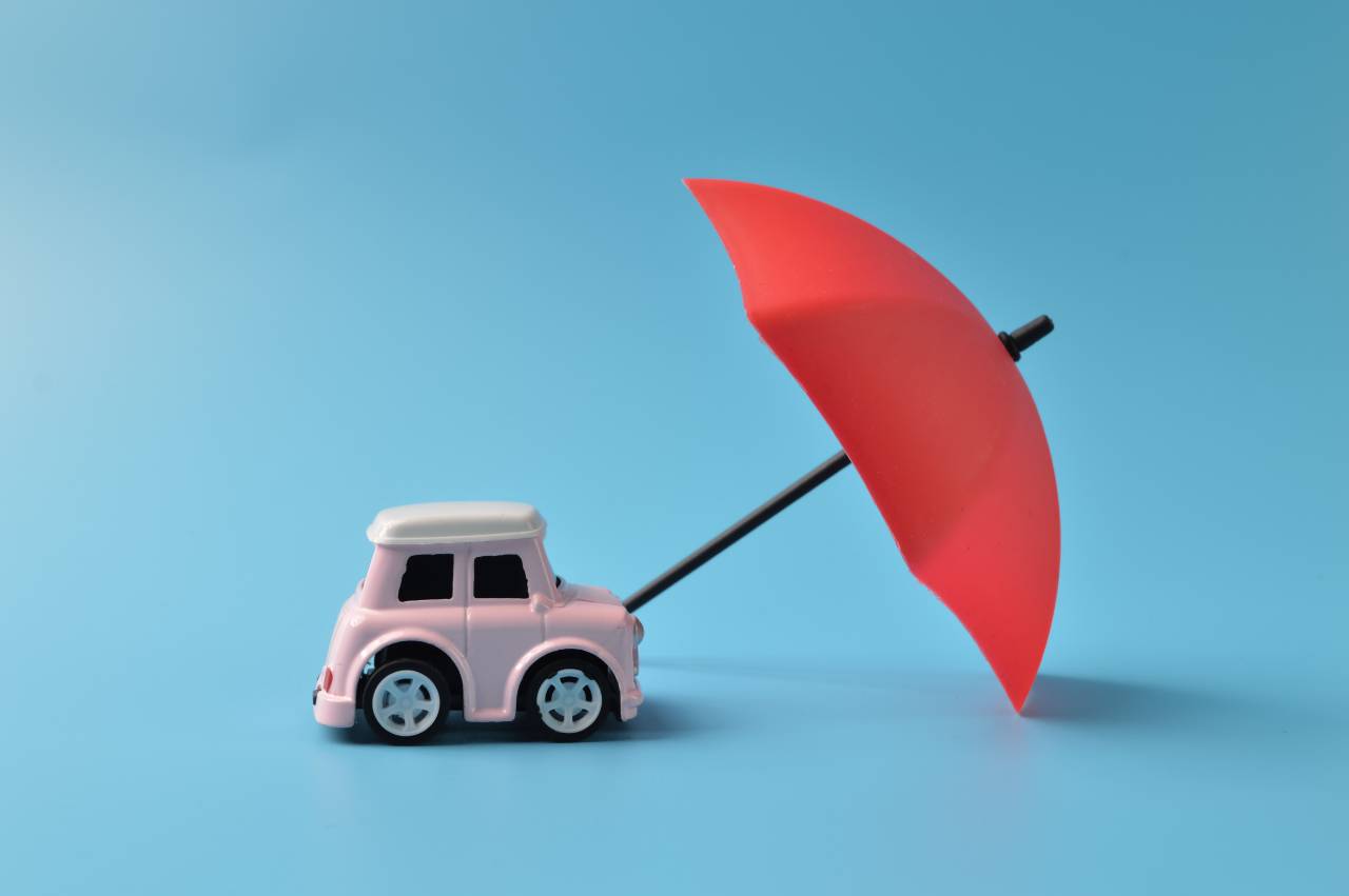 voiture protégée par un parapluie sur fond uni bleu