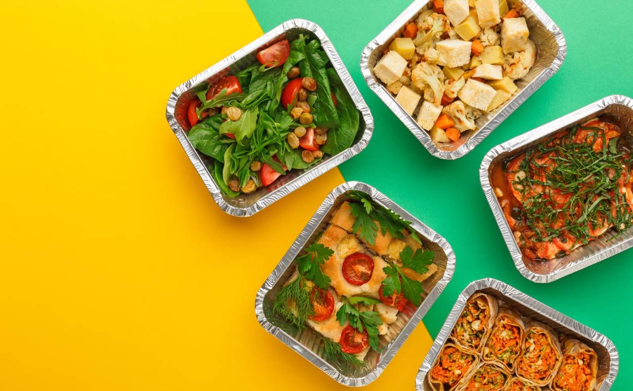 différents plats en barquettes aluminium exposés sur un fond jaune et vert